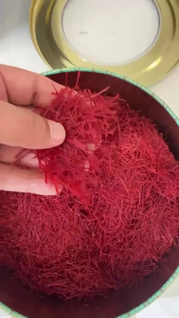 Hand checking saffron threads in a round tin beside its gold lid